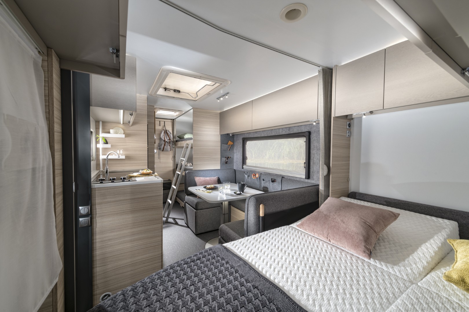 Intérieur de la caravane avec lit fixe à l’avant, coin repas au centre et lits superposés à l’arrière.