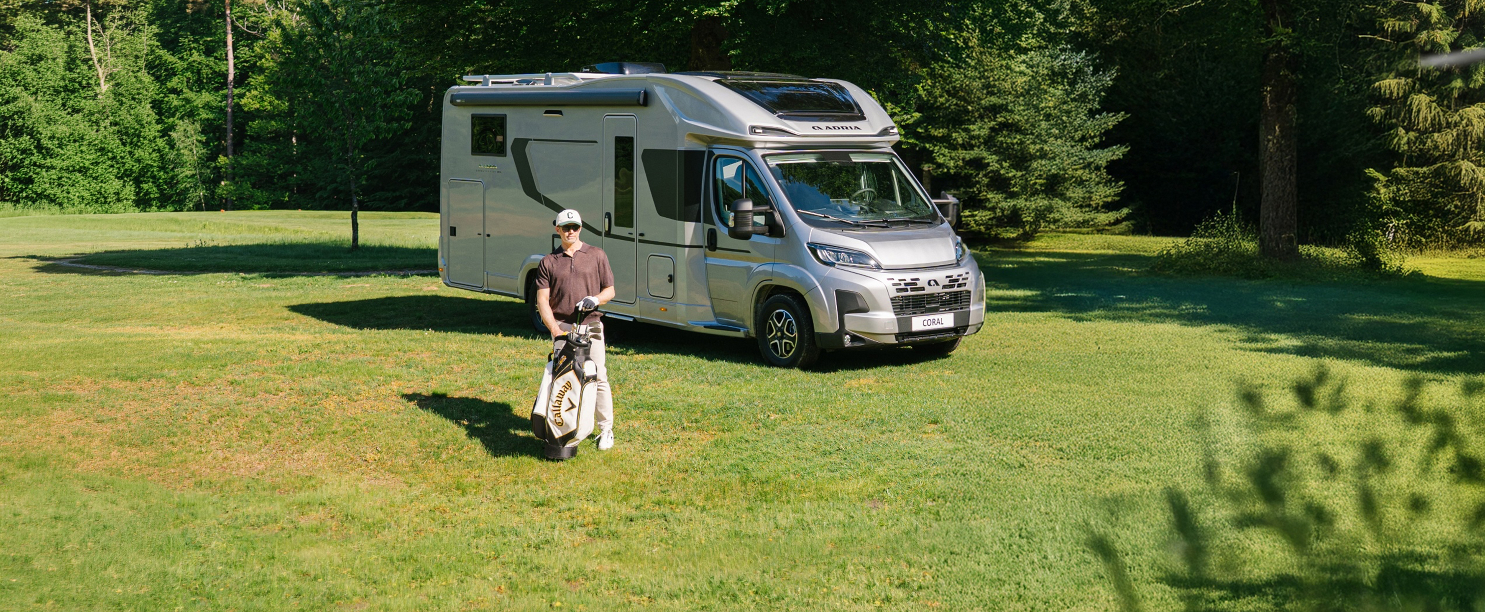 Das ADRIA CORAL Wohnmobil mit doppeltem Panoramadachfenster auf einem Golfplatz.