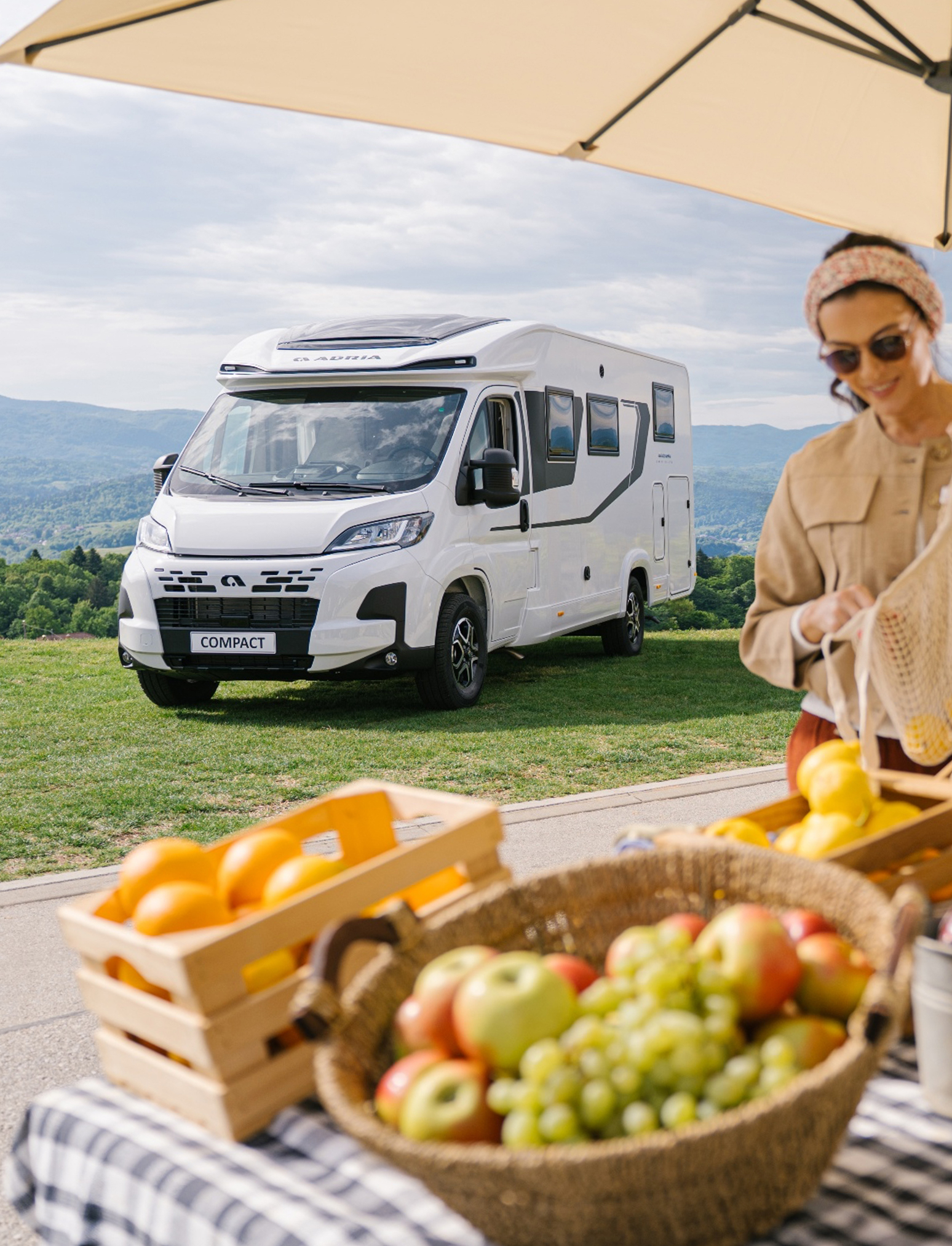 Der kompakte ADRIA COMPACT, ein Wohnmobil für 2 Personen, auf einer Wiese vor einer Berglandschaft.