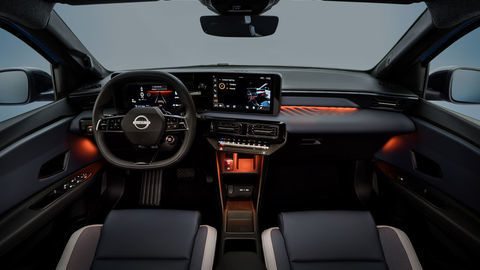 Thumb dimmed interior of micra dashboard and cockpit from driver s pov revealing orange ambient lighting by side doors  on dashboard and below air conditioning buttons.  steering wheel  front seats and infotainment in view