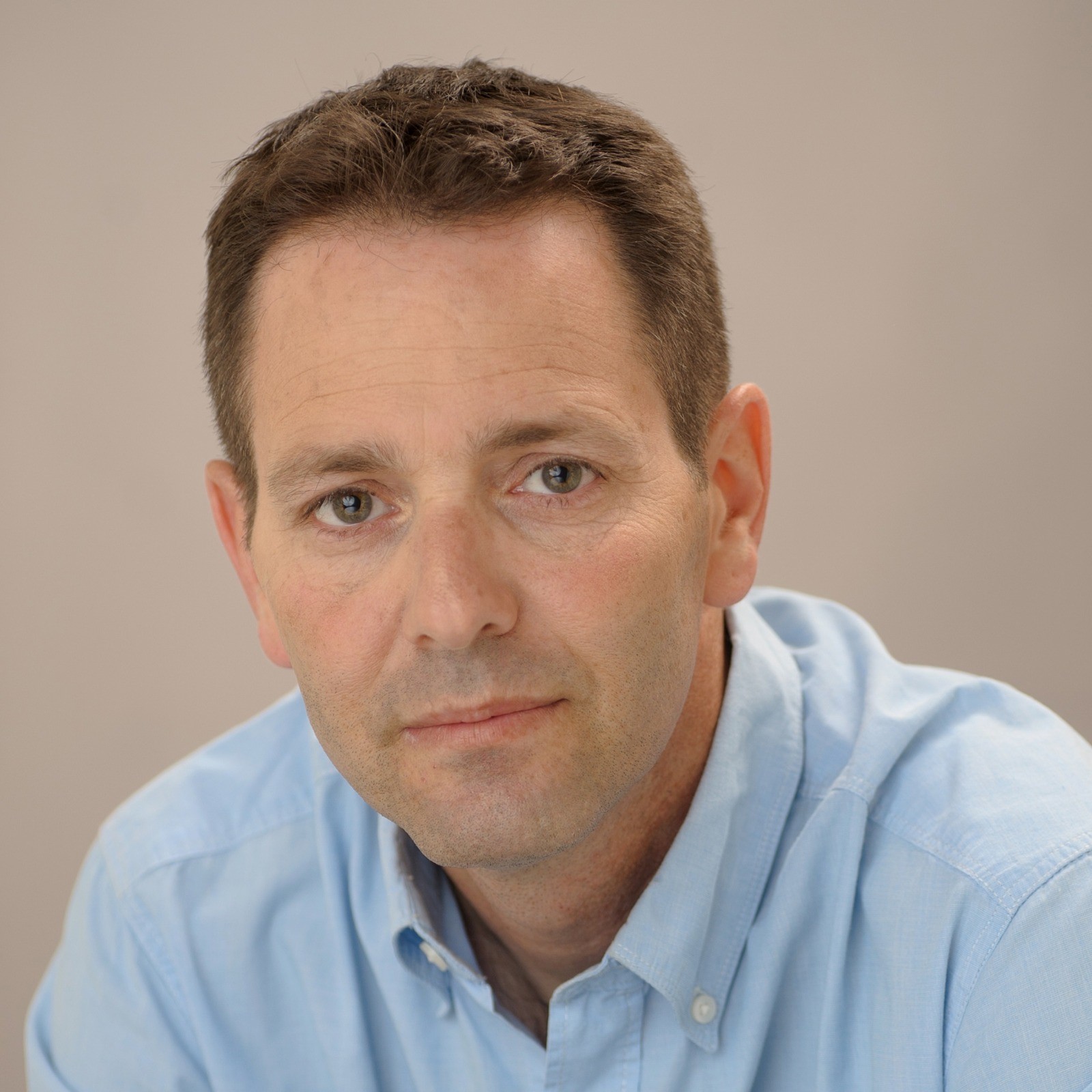 Professional headshot of a middle-aged man wearing a light blue button-up shirt