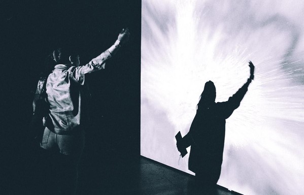 a scan of a black and white photo of a woman lifting her arm and looking at her shadow on a screen at an exhibit at the Getty museum in LA