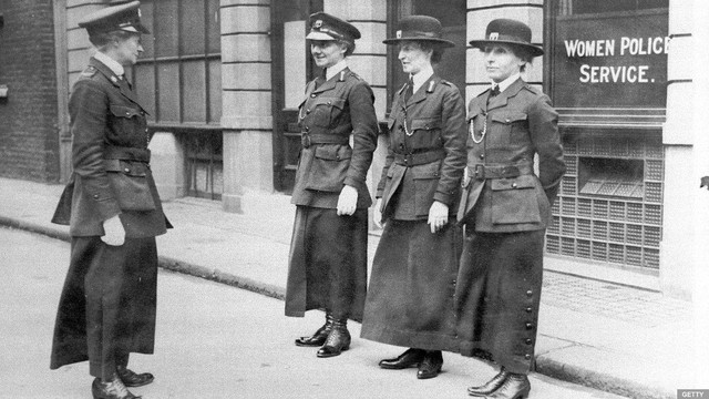 Photo of three WPV women being inspected by another woman, an officer. Mary Allen is on the far left in a peaked cap. All the women are white.