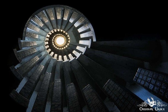 Spiral staircase viewed from below, with light shining through the center and vertical steps illuminated along the edges.