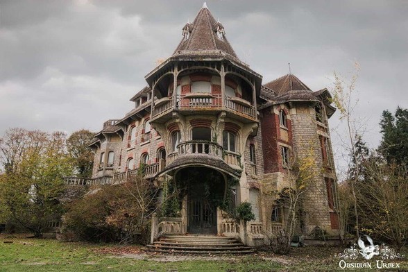 An abandoned three-story mansion with overgrown vegetation, decaying balconies, and a turreted roof under a cloudy sky.