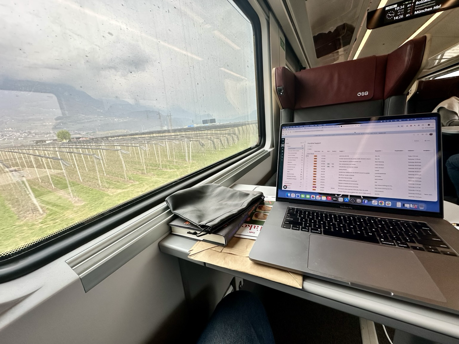 Picture of a view from a seat on a train with Italian landscape out the window and laptop on table in front of the passenger.