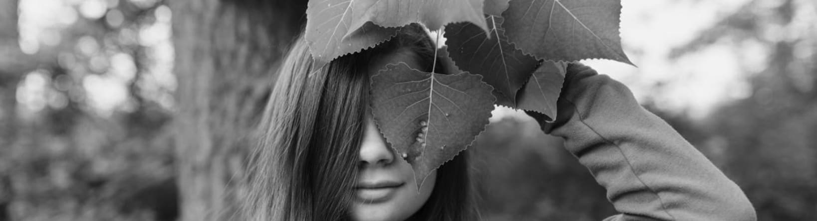 Woman with green leaves covering part of her face, in a natural setting, symbolising sustainability and respect for nature.