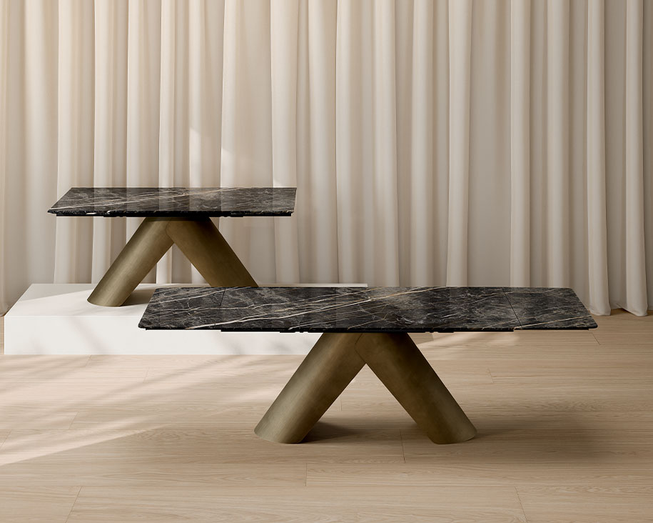 Couchtische mit dunkel geäderter Steinzeugplatte in Marmoroptik und goldenen zylindrischen Untergestellen vor einem Hintergrund aus beigen Vorhängen.