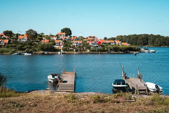 A scenic view of a coastal village featuring numerous red-roofed houses amidst green trees, bordering a calm blue sea.…