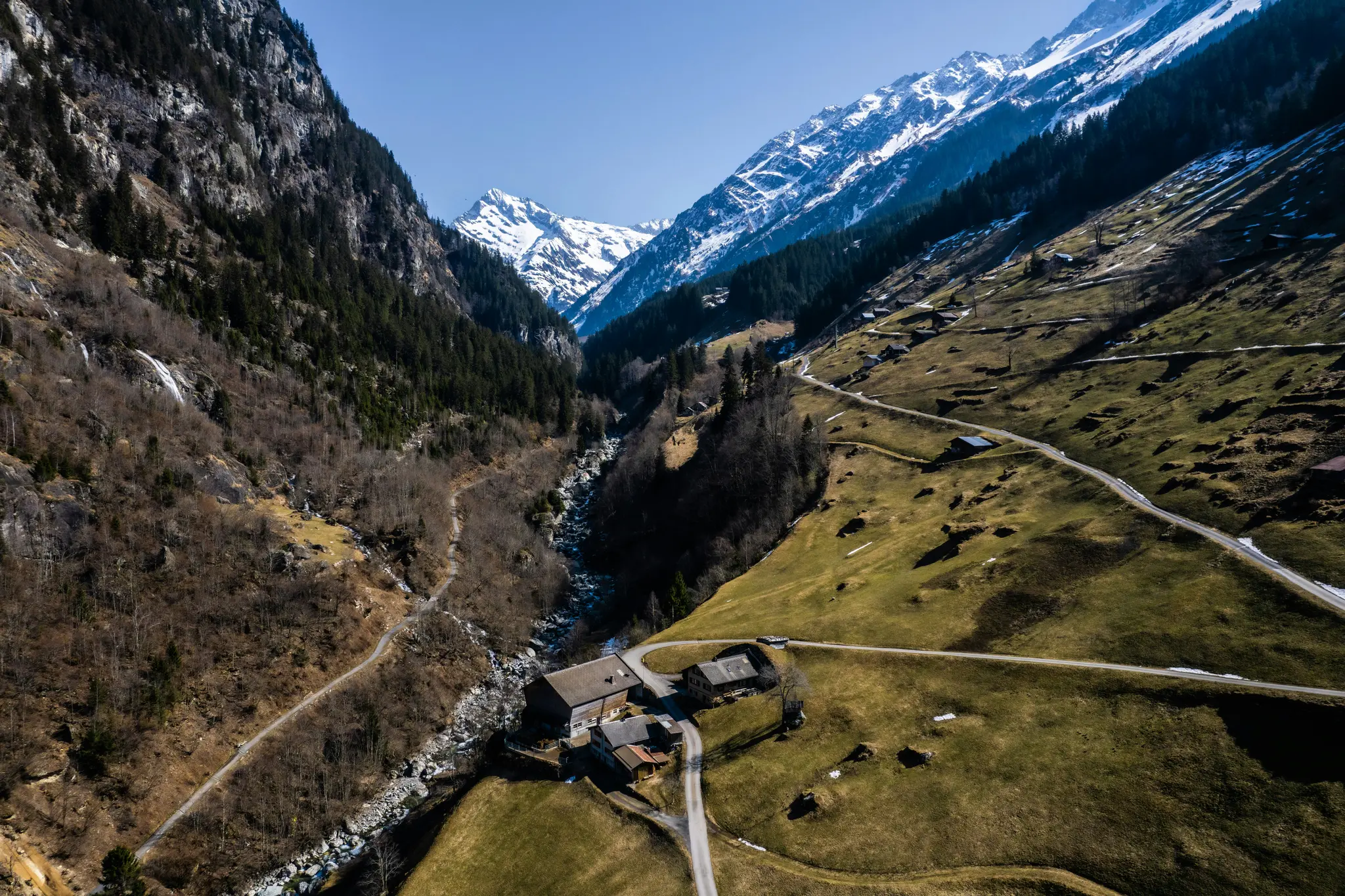 An aerial view of a deep valley with a river flowing through it, surrounded by steep, forested mountainsides. Several…
