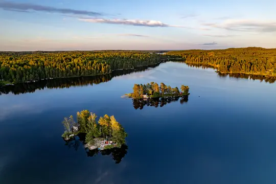 En flygbild av en lugn, djupt blå sjö som reflekterar det gyllene ljuset från den nedgående solen. Två små öar med träd
