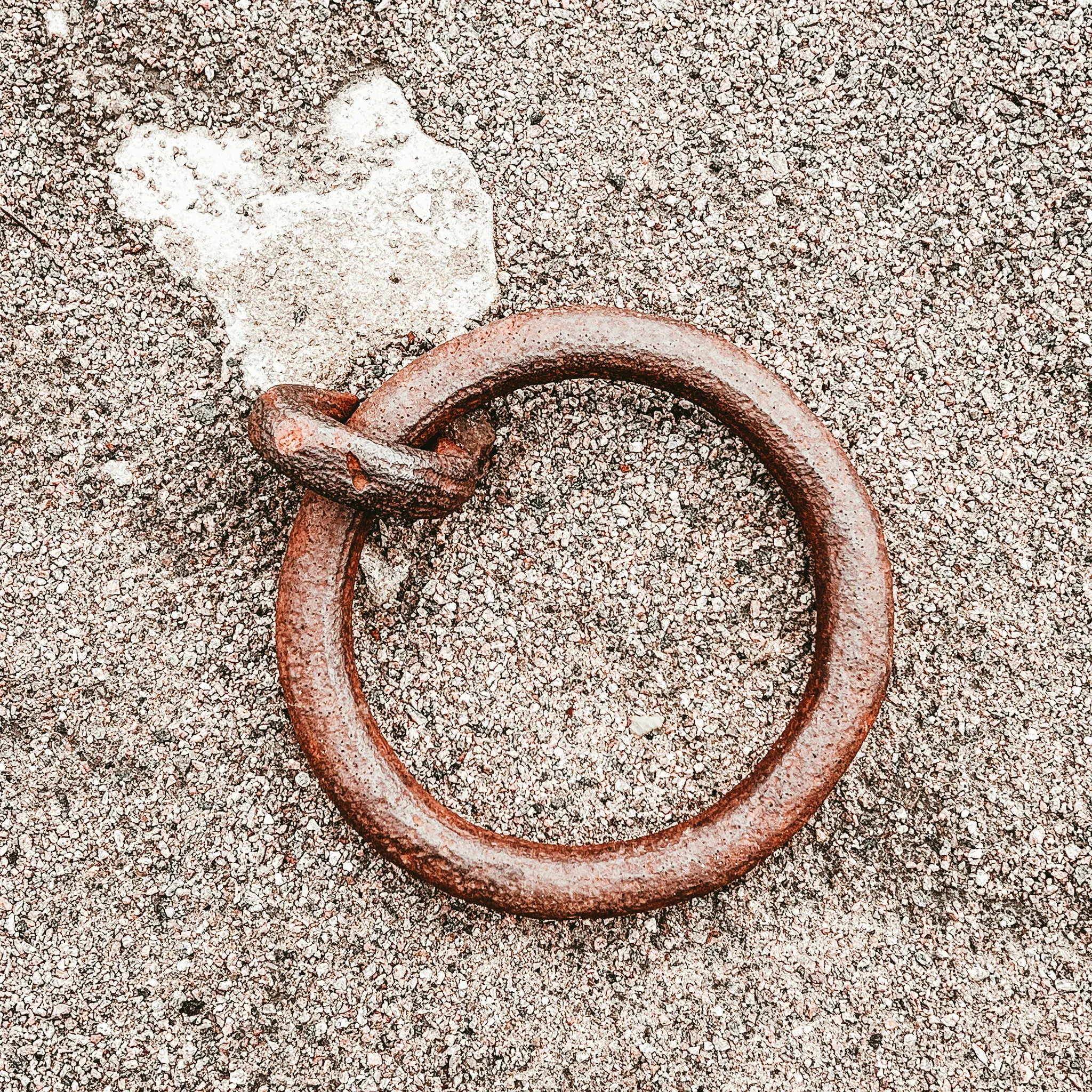 En närbild, sedd ovanifrån, av en kraftigt rostig, tjock metallring som delvis är nedsänkt i en texturerad grusyta.