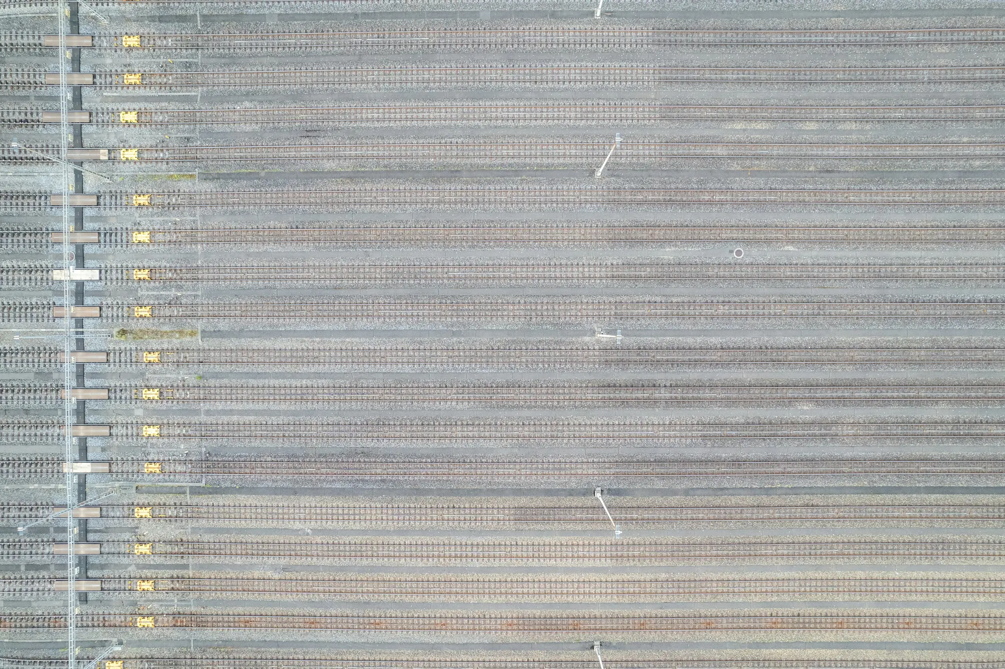 An aerial, top-down view of a vast train yard with many parallel tracks on grey gravel, some with yellow elements.