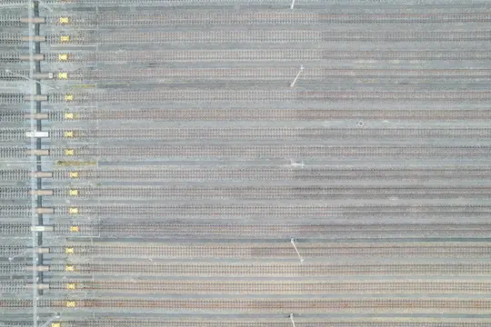 An aerial, top-down view of a vast train yard with many parallel tracks on grey gravel, some with yellow elements.