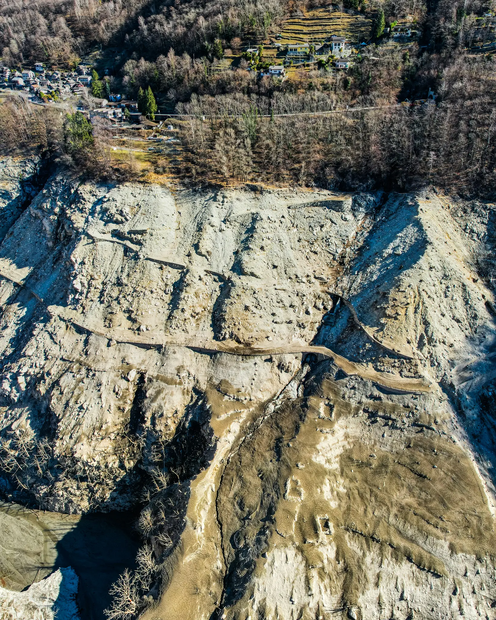 An aerial shot captures a rugged, eroded hillside with a winding path, leading up to a village nestled among trees.