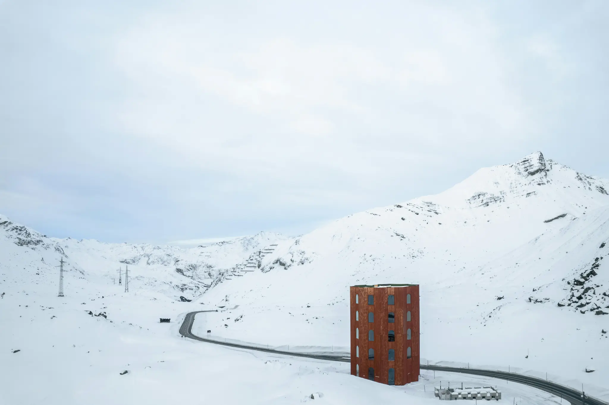 Una vista aérea de un edificio alto de color óxido con múltiples ventanas junto a una carretera sinuosa en una vasta zona