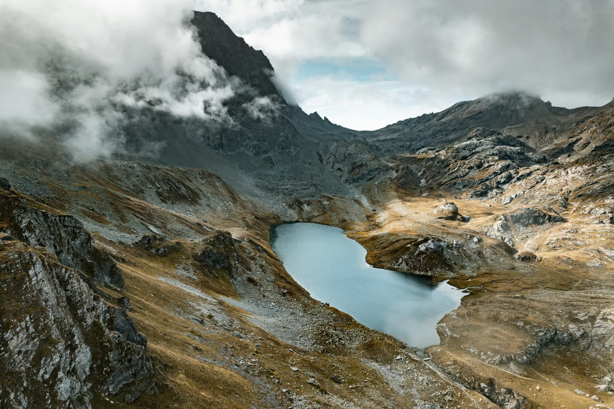 Una vista aérea muestra un sereno lago azul de montaña enclavado entre empinadas laderas rocosas y terreno árido bajo un
