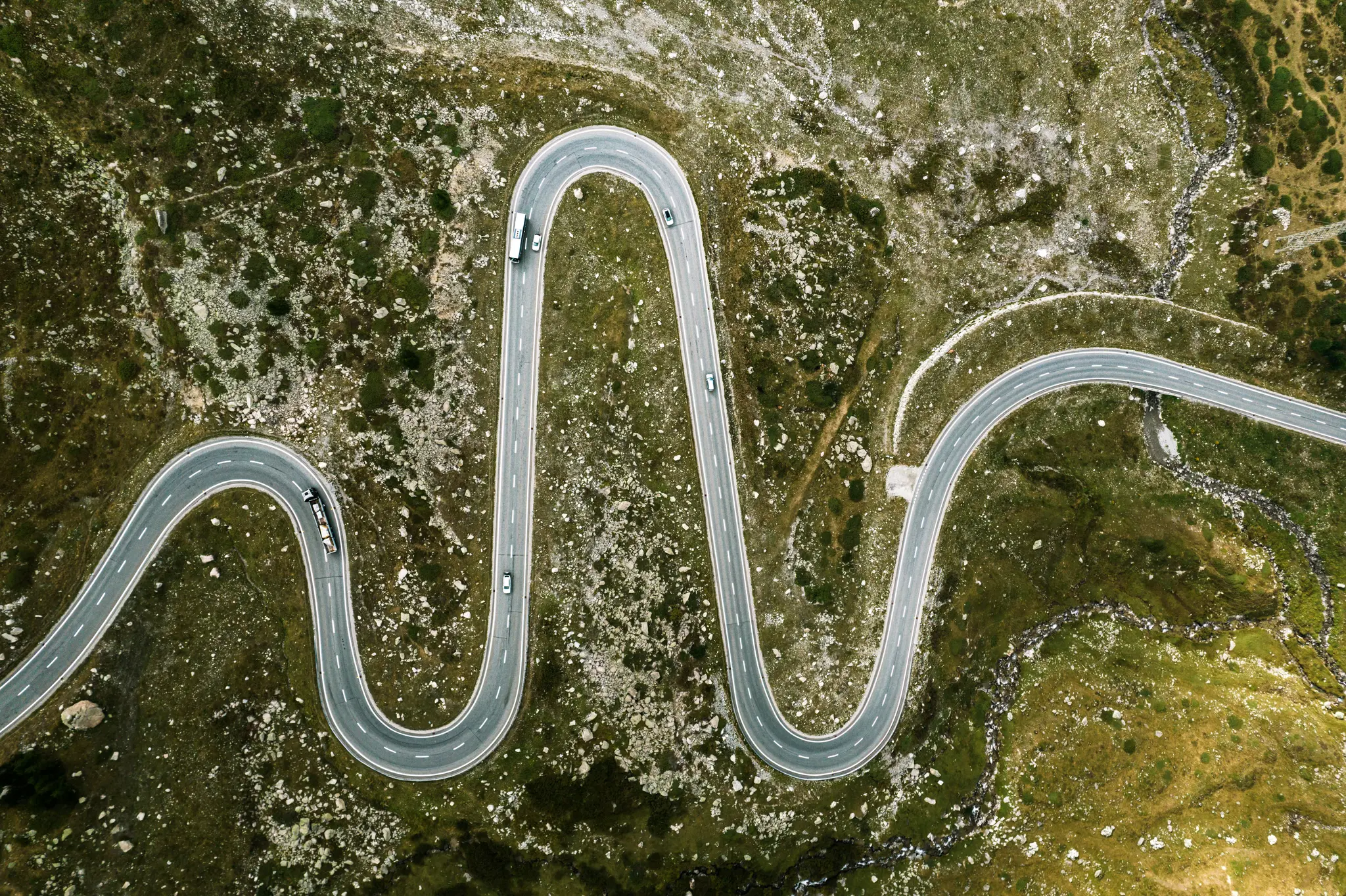 Una vista aérea muestra una carretera gris y sinuosa con líneas blancas que serpentean a través de un paisaje montañoso verde