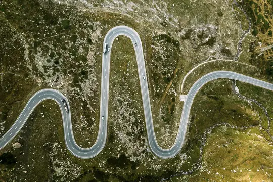 Una vista aérea muestra una carretera gris y sinuosa con líneas blancas que serpentean a través de un paisaje montañoso verde