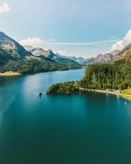 Una vista aérea de un lago vasto y azul profundo que refleja el cielo, bordeado por exuberantes bosques verdes y montañas