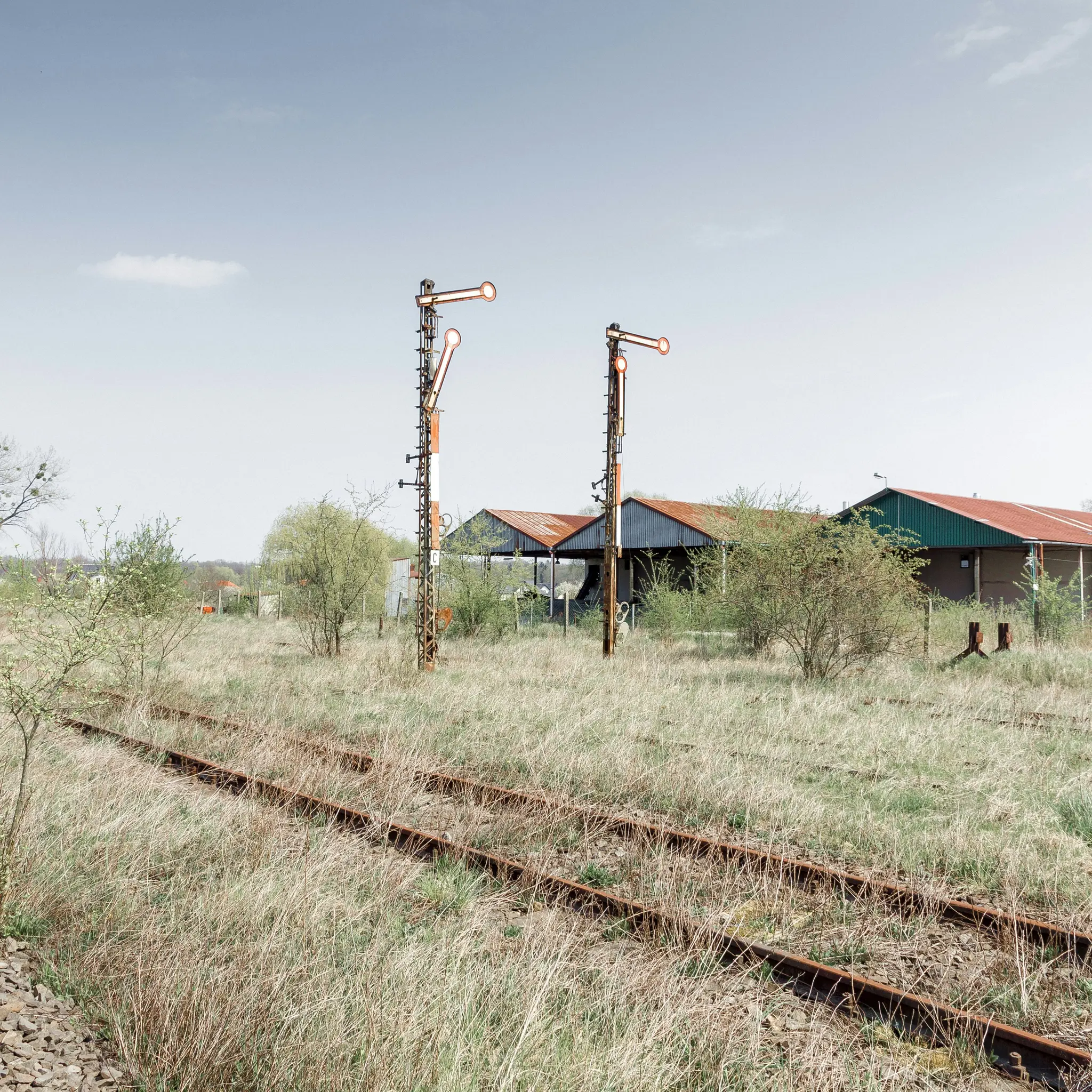 Eine Weitwinkelaufnahme einer verlassenen, mit trockenem Gras bedeckten Eisenbahnschiene, die zu zwei hohen, rostigen