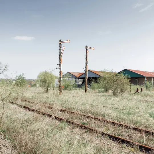 Una toma amplia de una vía de tren abandonada cubierta de hierba seca, que conduce a dos señales de ferrocarril altas y