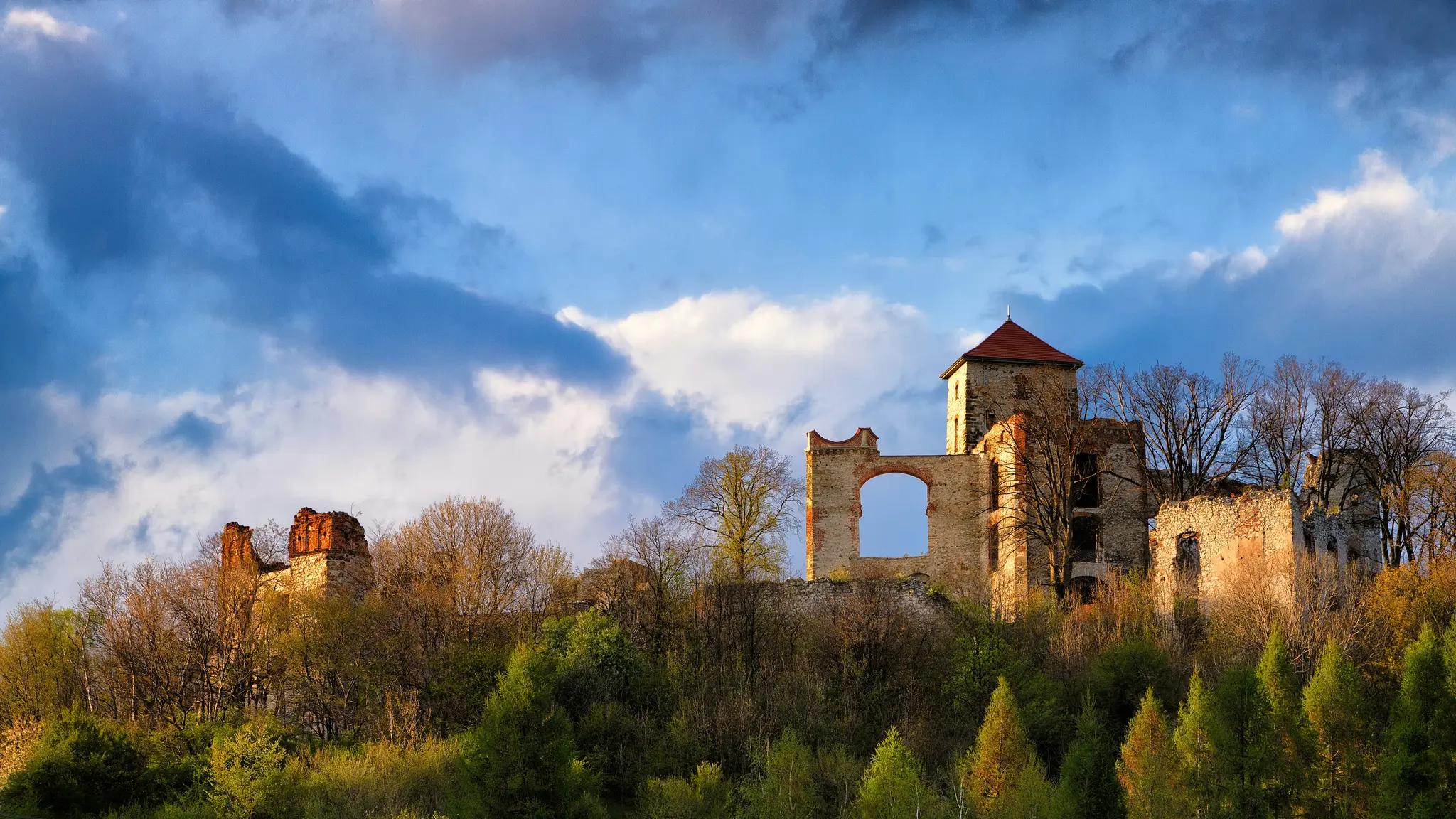 Una vista panorámica amplia de una ruina de castillo de piedra antigua con una torre prominente y techo rojo, rodeada de
