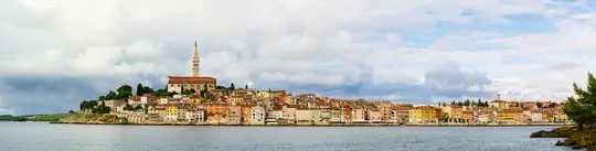 Et bredt panoramabillede af en levende kystby med mange farverige bygninger samlet på en halvø, toppet af en høj…