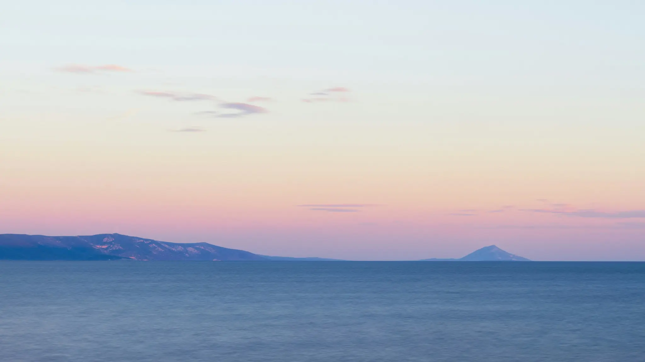 Una amplia foto de paisaje que muestra un mar tranquilo de color azul profundo bajo un cielo que transita del azul claro al