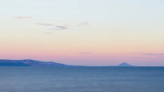 Una amplia foto de paisaje que muestra un mar tranquilo de color azul profundo bajo un cielo que transita del azul claro al