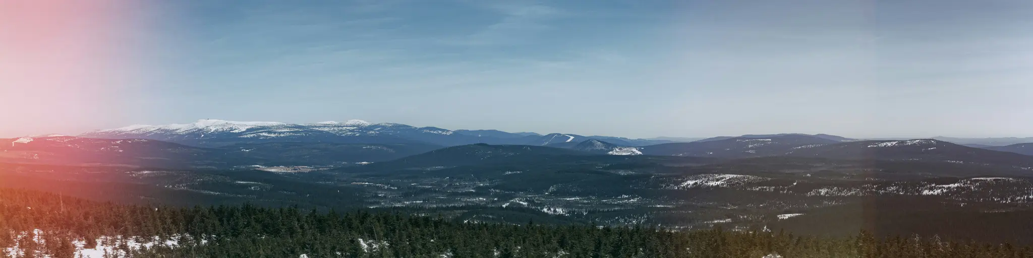 Una toma panorámica amplia de una cordillera invernal. Los picos nevados se elevan en la distancia, con bosques verde oscuro