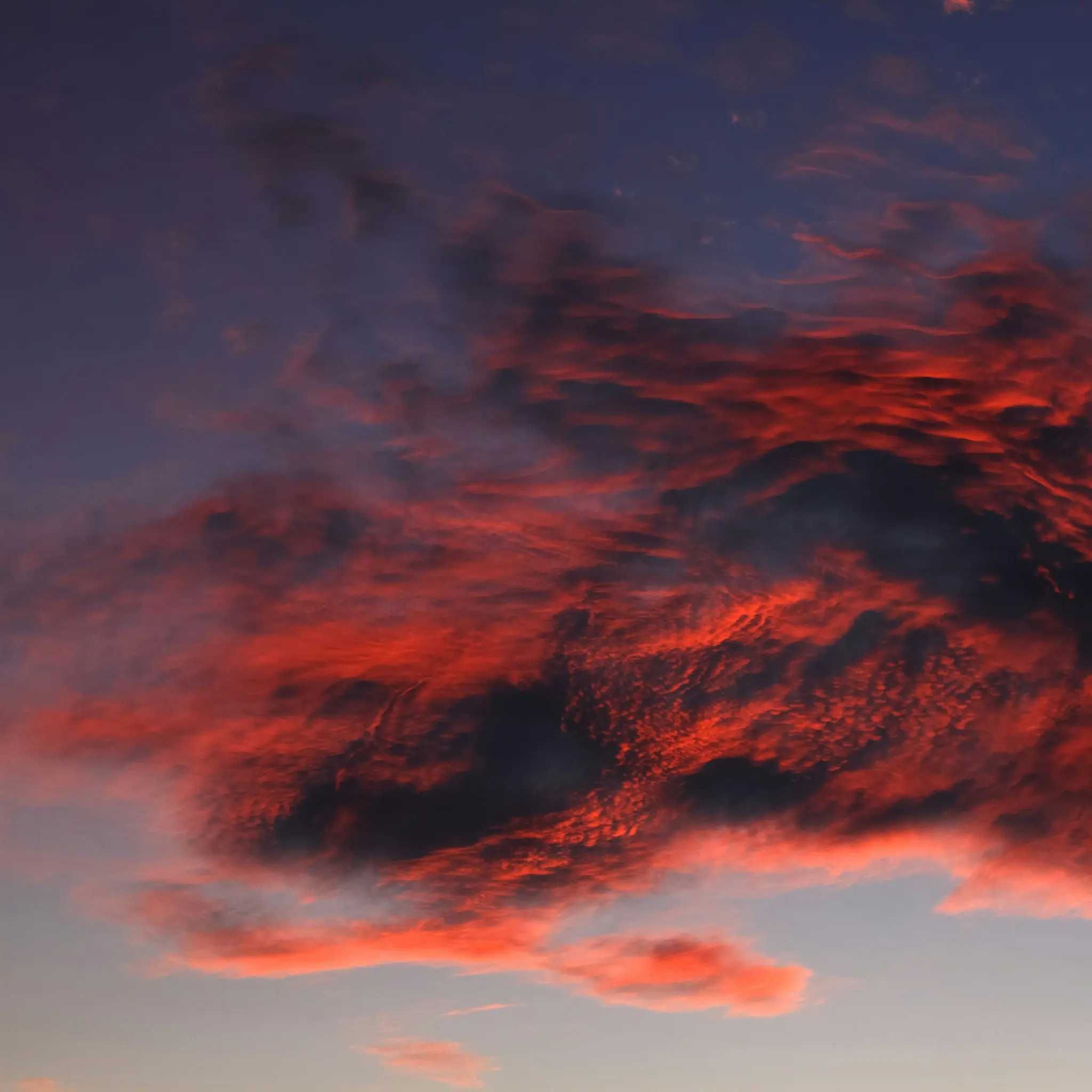 Ein dramatischer Himmel bei Sonnenuntergang oder Sonnenaufgang mit dunklen Wolken, die intensiv mit leuchtenden Rot- und