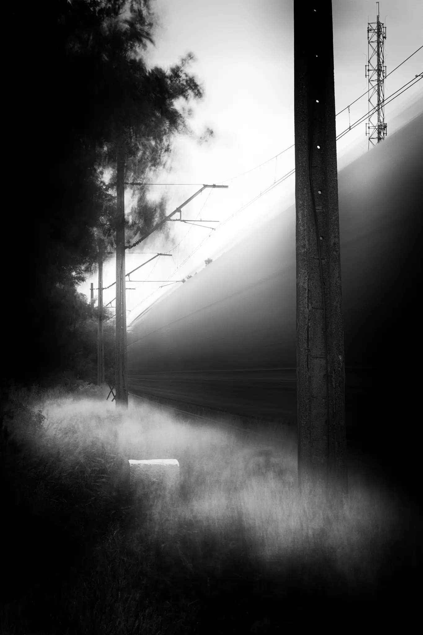 Ein Schwarz-Weiß-Foto zeigt einen Zug als verschwommenen Licht- und Schattenstreifen, der an Stromleitungen und einem