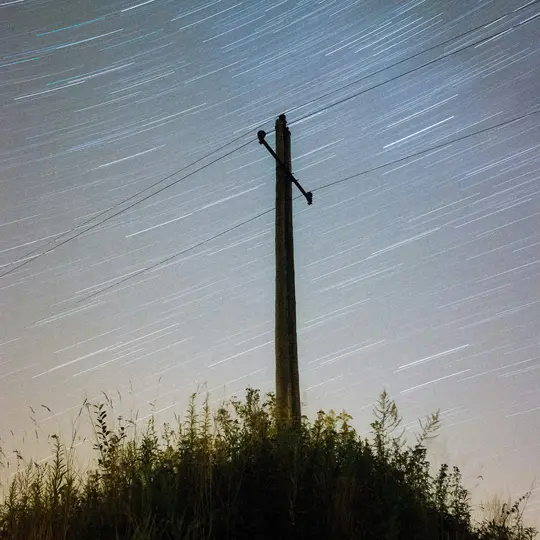 Una foto de larga exposición muestra rastros de estrellas blancos cruzando un cielo nocturno azul oscuro sobre un poste de