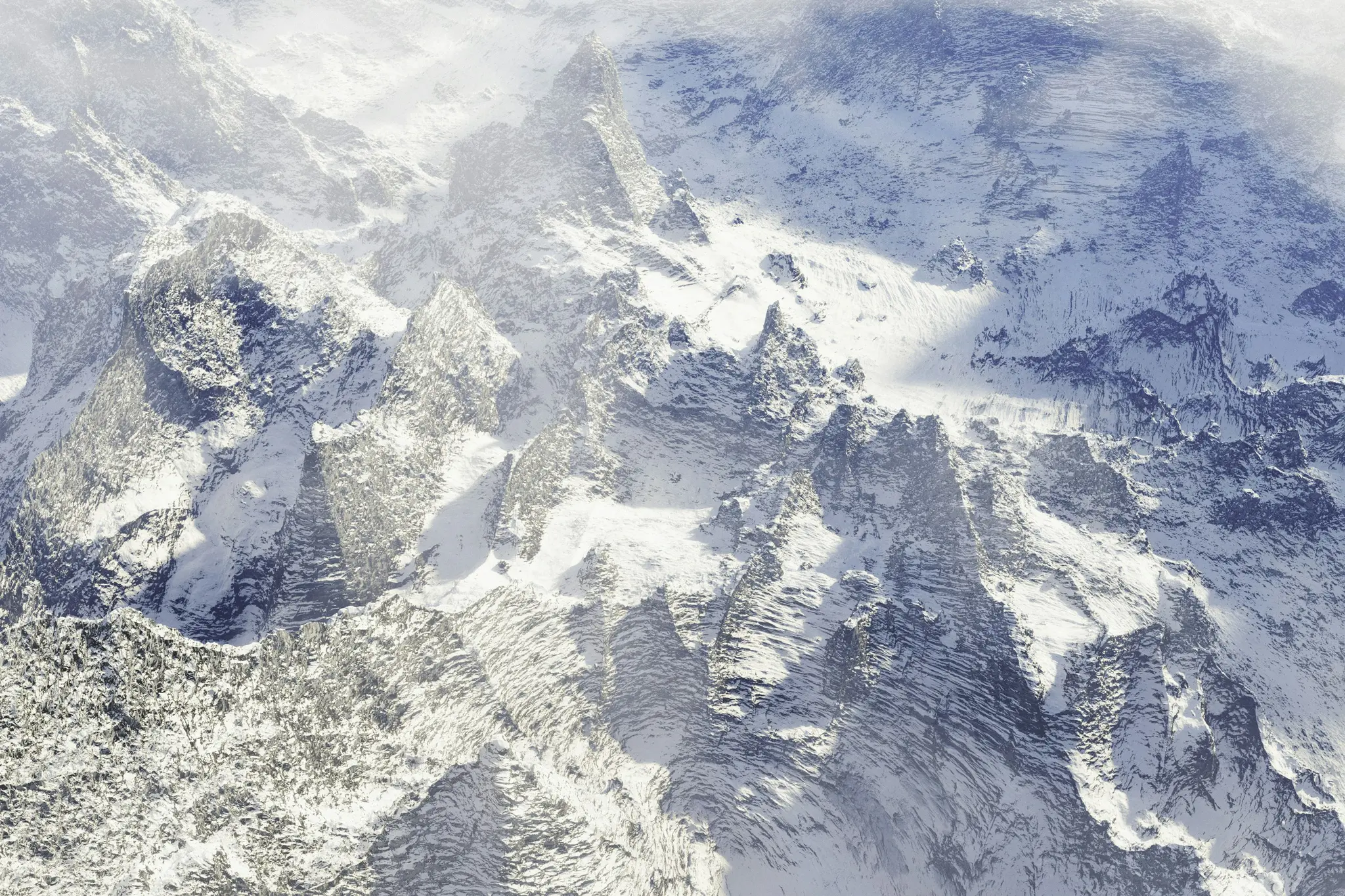 Eine Luftaufnahme zeigt eine weite Fläche von schneebedeckten Berggipfeln und zerklüfteten Graten unter einem bedeckten