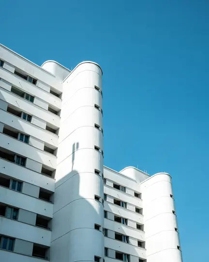 Una ripresa dal basso di un edificio bianco moderno con sezioni curve e finestre rettangolari, che proietta ombre sotto un