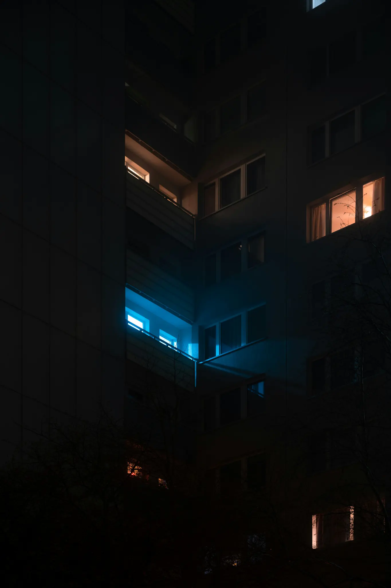 Una fachada de edificio oscura de noche, con varias ventanas brillantes. Una ventana emite una luz azul brillante, otras