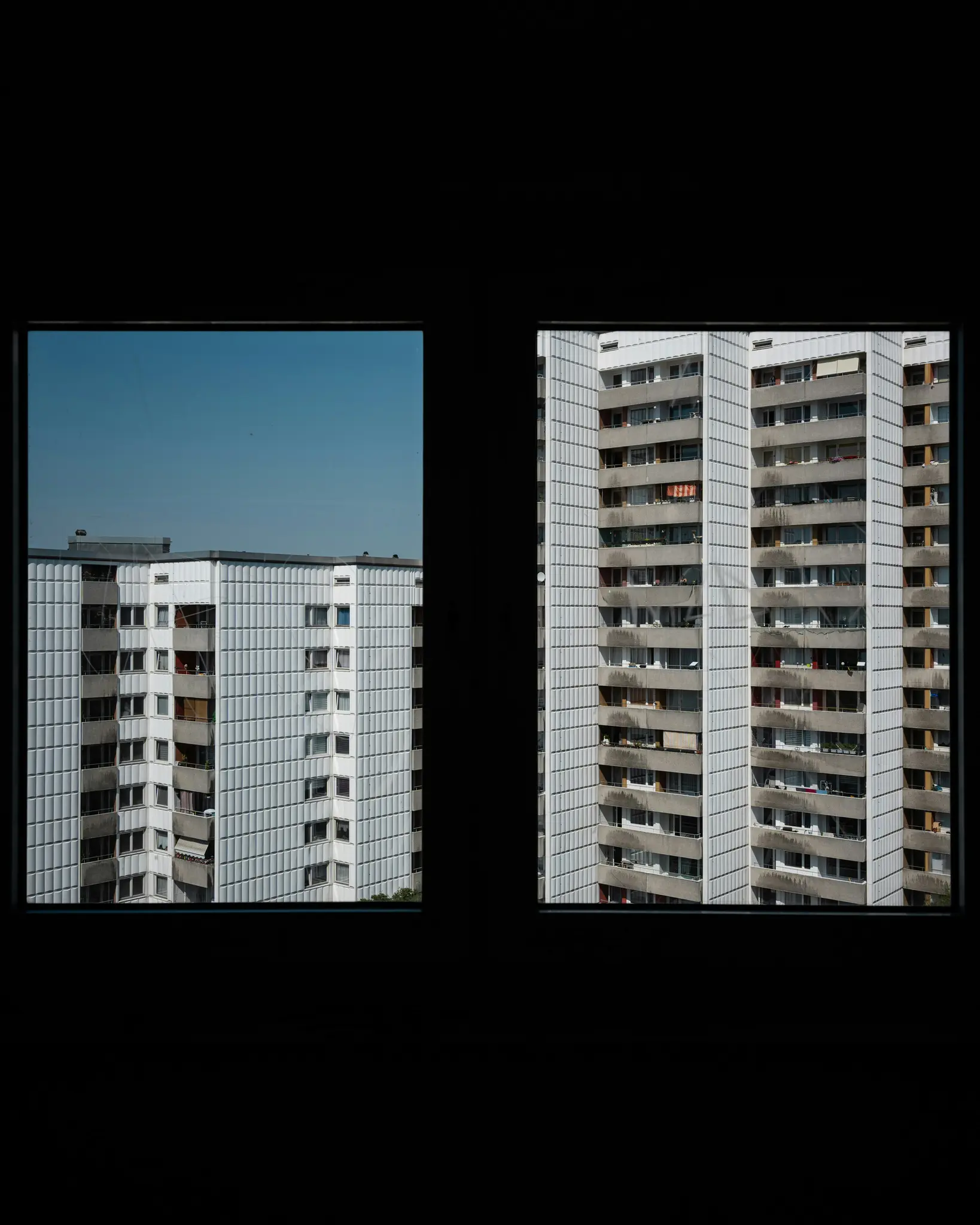 Una vista a través de dos cristales de ventana oscuros que muestran partes de dos edificios de apartamentos grandes, blancos