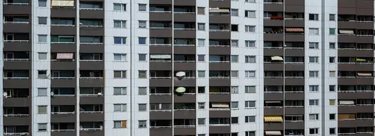 Detailní záběr celé fasády vysokého obytného domu s mnoha okny a balkony.