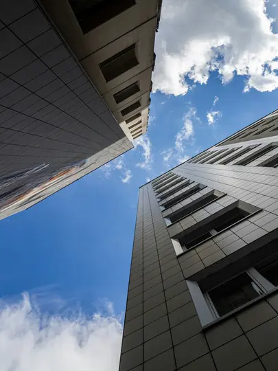 A low-angle shot of three tall buildings with modern facades against a bright blue sky with scattered white clouds.