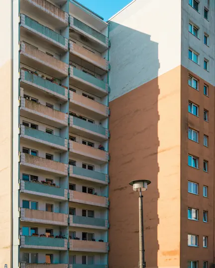 Uno scatto verticale di due alti edifici con appartamenti. Uno ha balconi beige e azzurri, l'altro è arancione-marrone. Un…