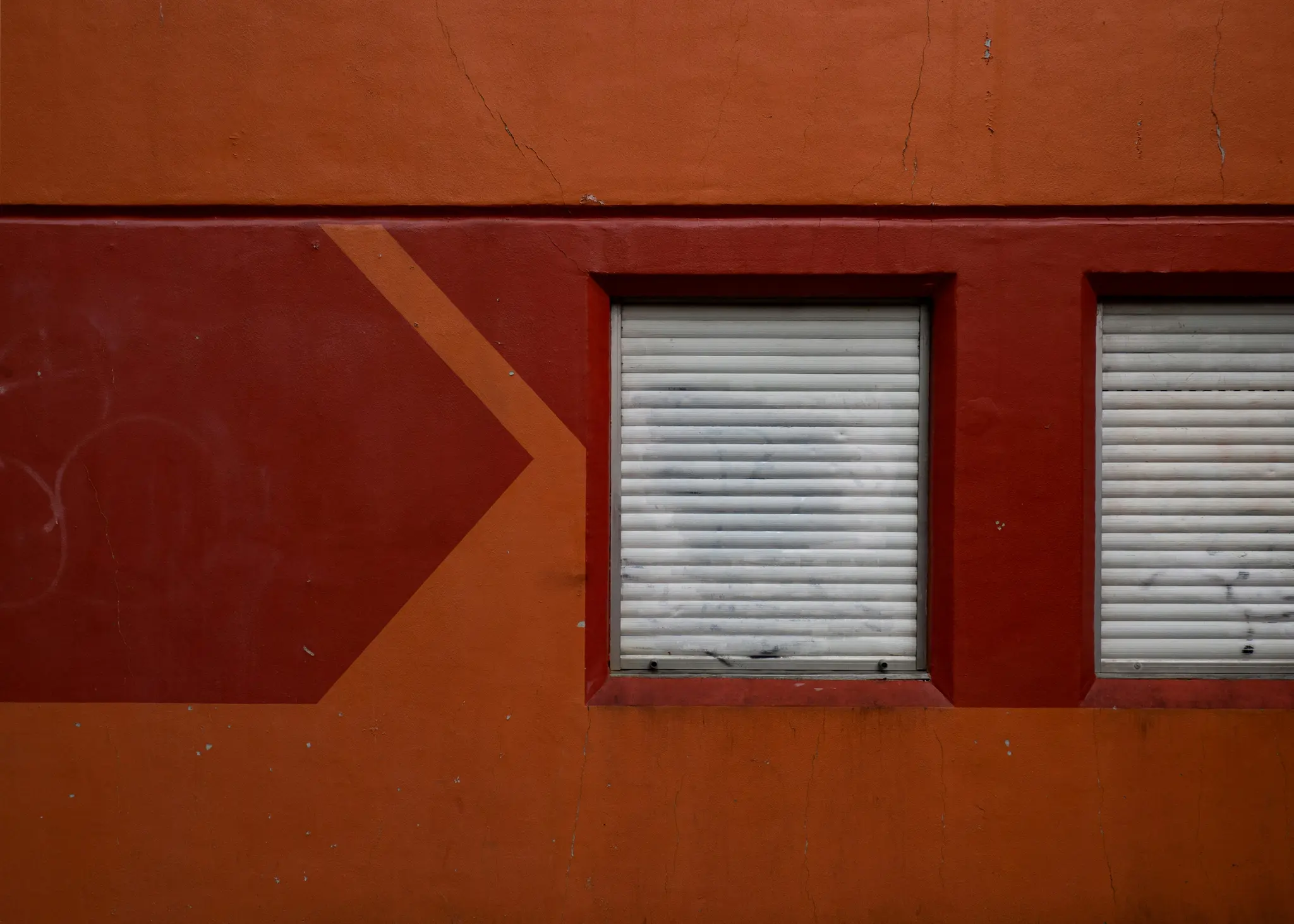 Primer plano de la pared de un edificio pintada en tonos naranjas y rojos, con dos ventanas con persianas blancas.