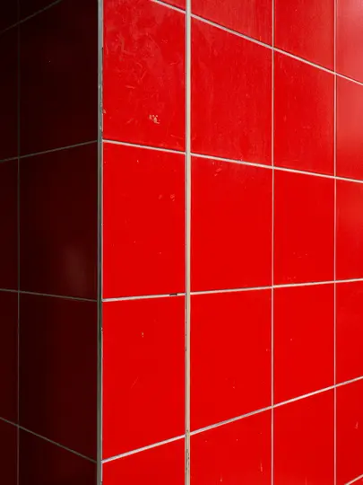 Un primo piano di un angolo dove si incontrano due pareti, entrambe ricoperte da piastrelle quadrate rosso vivo con fughe