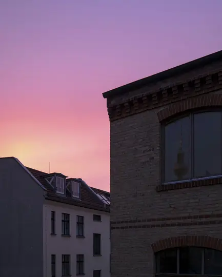 Ein lebendiger rosa und violetter Himmel in der Dämmerung oder im Morgengrauen über Stadthäusern. Die Reflexion eines Turms
