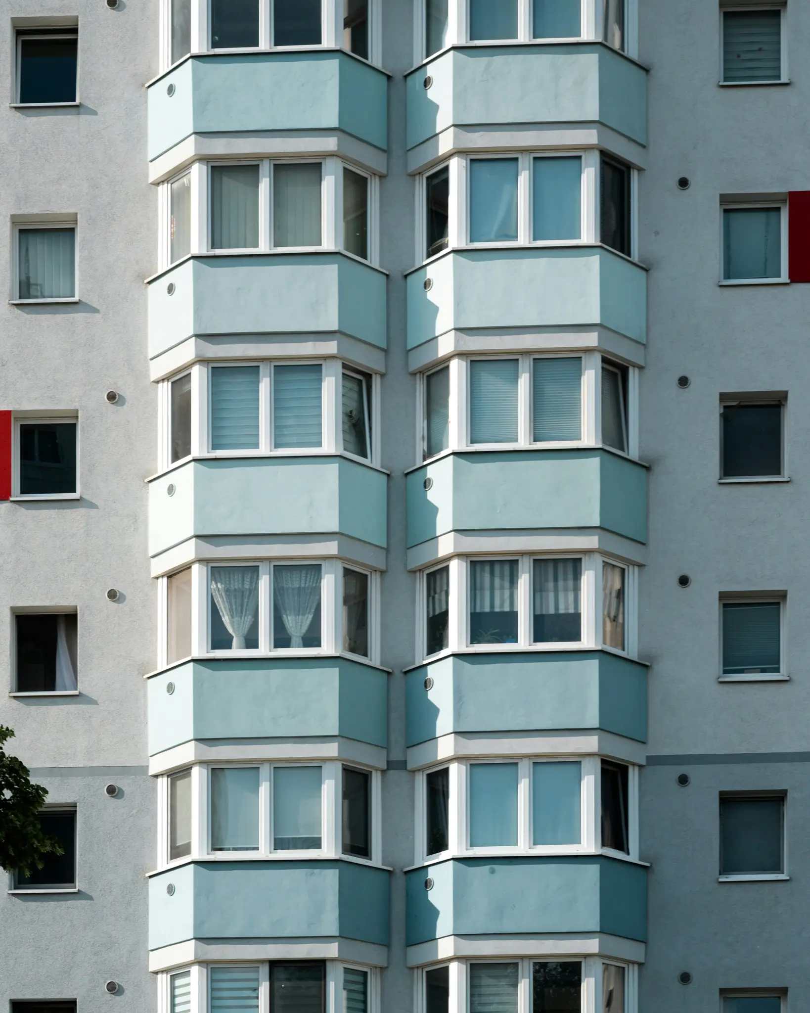 Un primer plano vertical de la fachada de un edificio con paredes de color gris claro y ventanales de color azul claro con