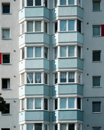 Un primo piano verticale della facciata di un edificio con pareti grigio chiaro e bow window blu chiaro con cornici bianche.