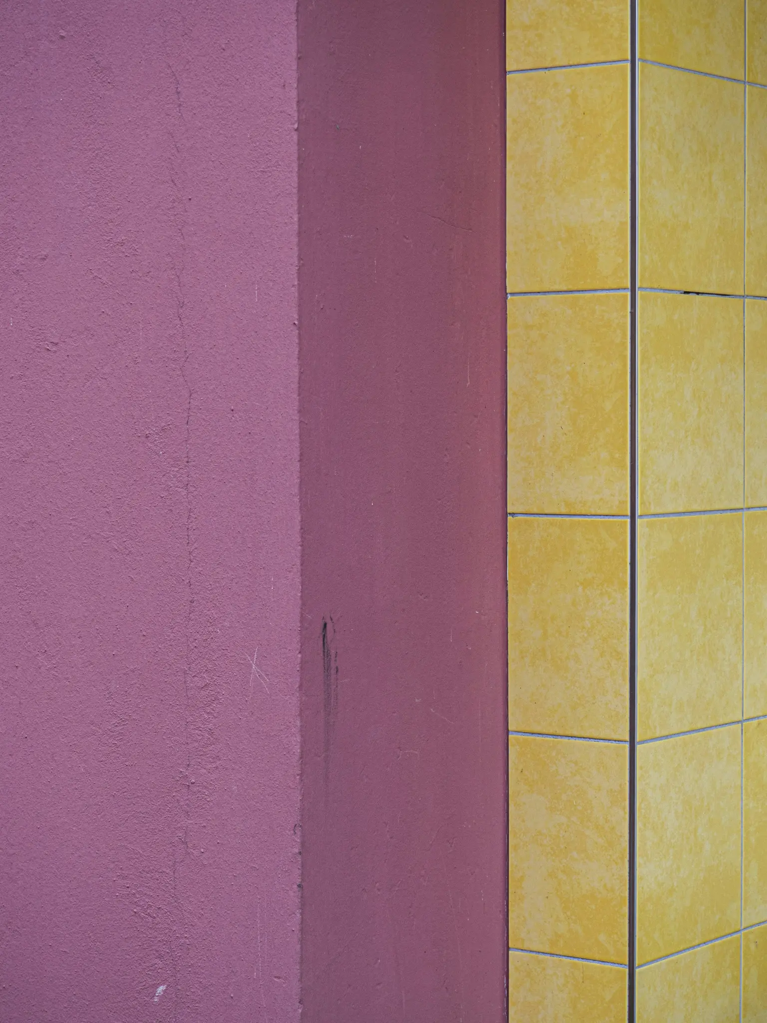Una vista cercana y abstracta de la esquina de un edificio. Una pared morada texturizada se une a una pared de azulejos