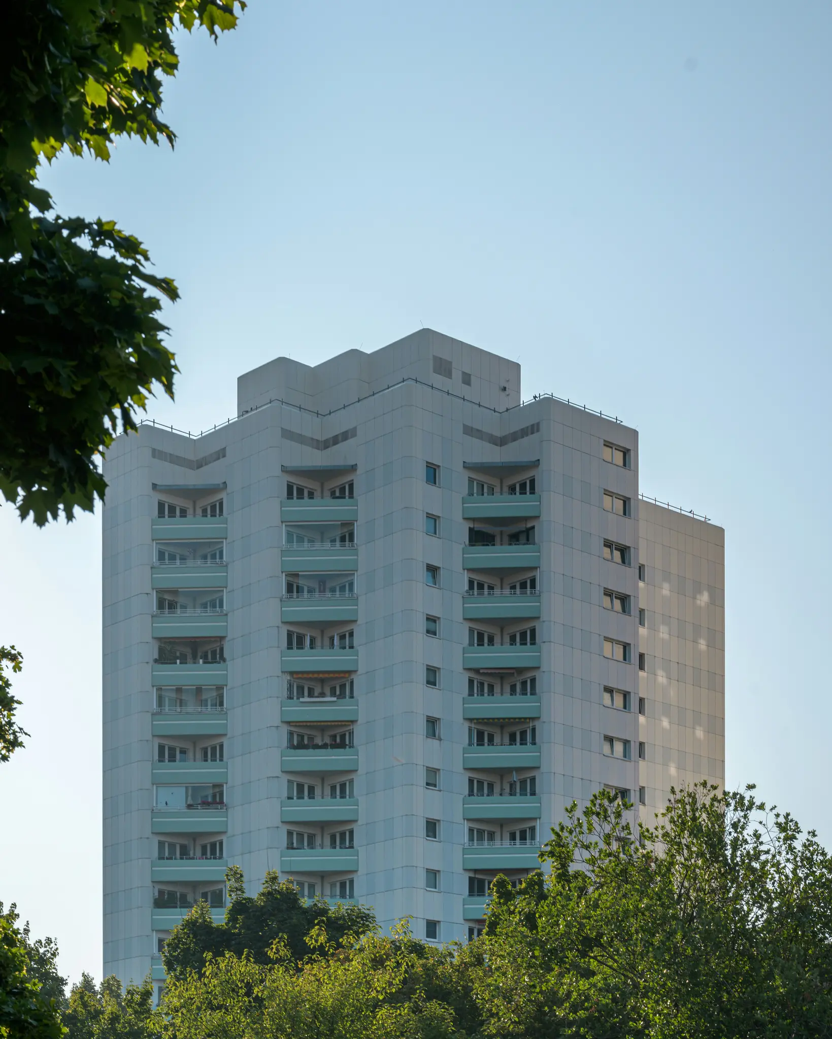 Un edificio residencial alto y de color claro con numerosos balcones de color teal se alza contra un cielo azul claro