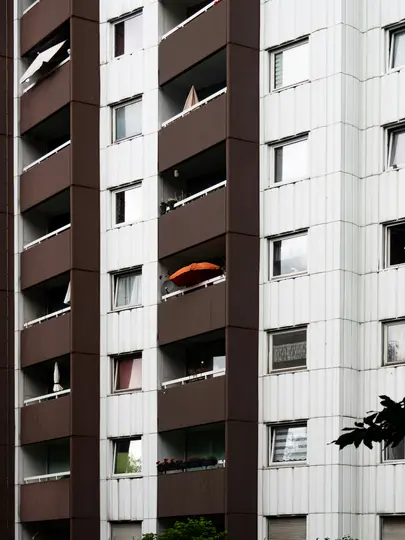Un primo piano verticale della facciata di un condominio, con balconi marroni e pareti bianche con numerose finestre.