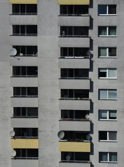 Una vista ravvicinata, frontale, di una facciata di edificio grigia con numerosi balconi e finestre. Diverse antenne